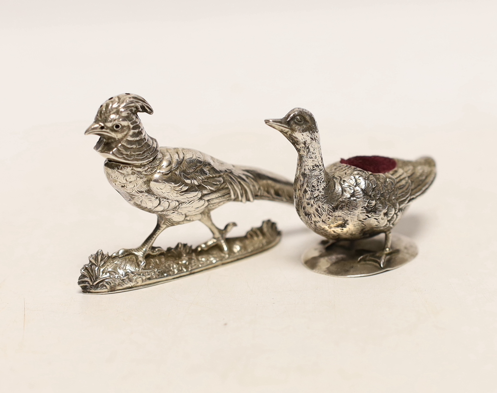 An early 20th century Hanau novelty silver pin cushion, modelled as a duck on circular base, import marks for Singleton, Benda & Co Ltd, length 64mm, together with a pepperette modelled as a pheasant, maker MF, Chester?,